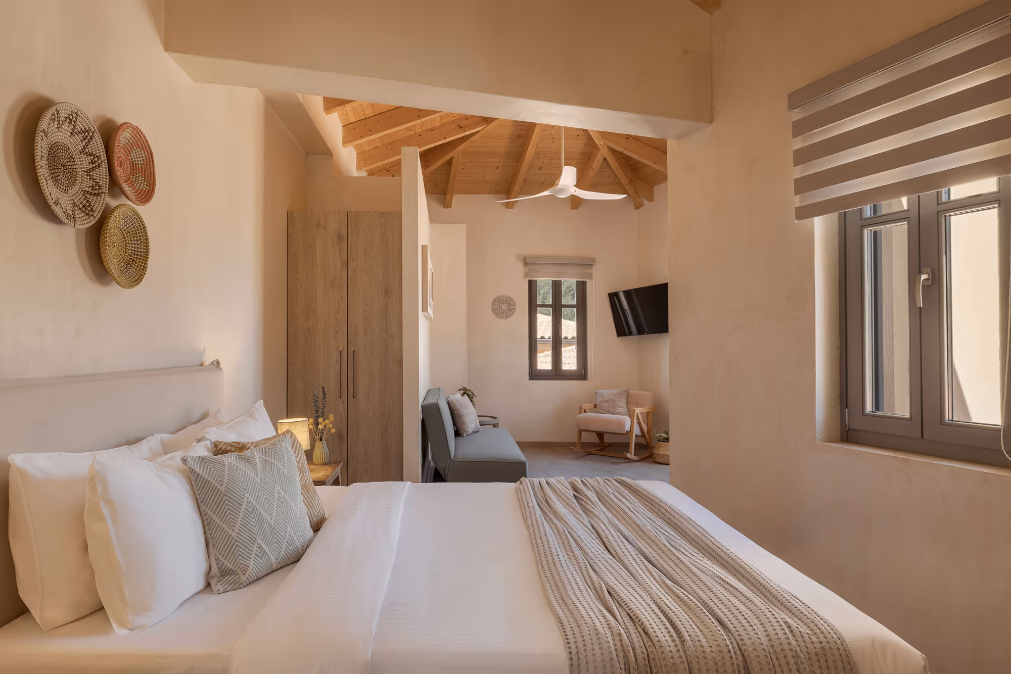Neutral-toned bedroom with a white bed, decorative pillows, woven wall art, and a wooden ceiling fan.
