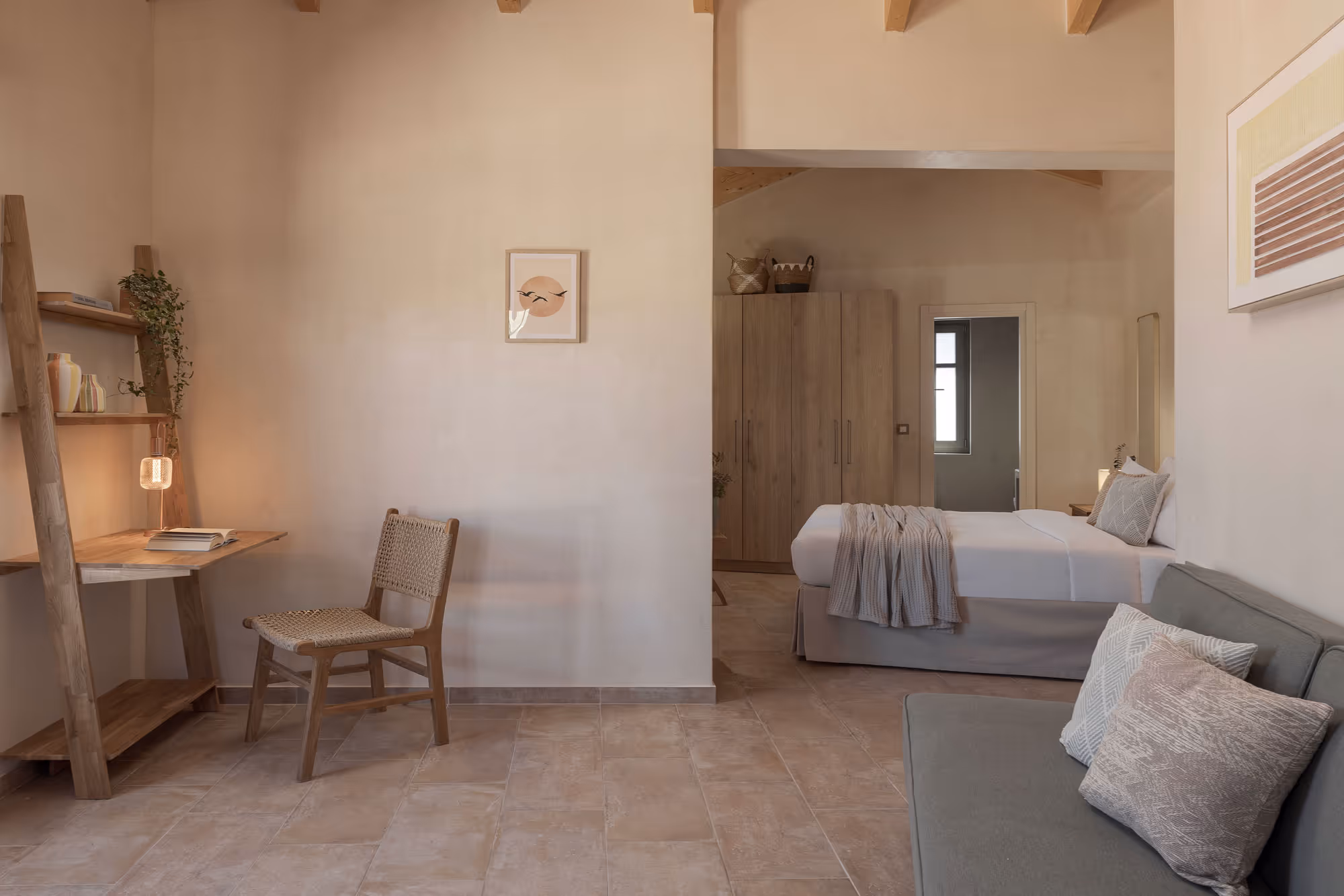 Minimal bedroom with a wooden chair, desk, bed, sofa, neutral decor, and tiled floor.