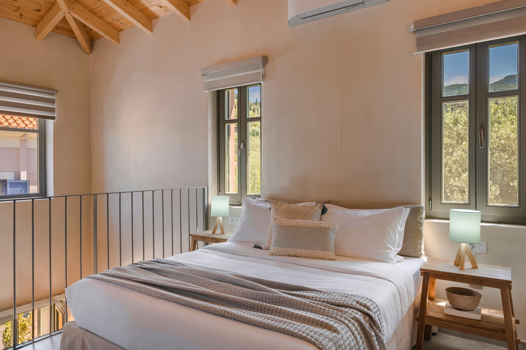 Cozy bedroom with wooden ceiling, double bed, neutral linens, two side tables, and windows showing greenery.