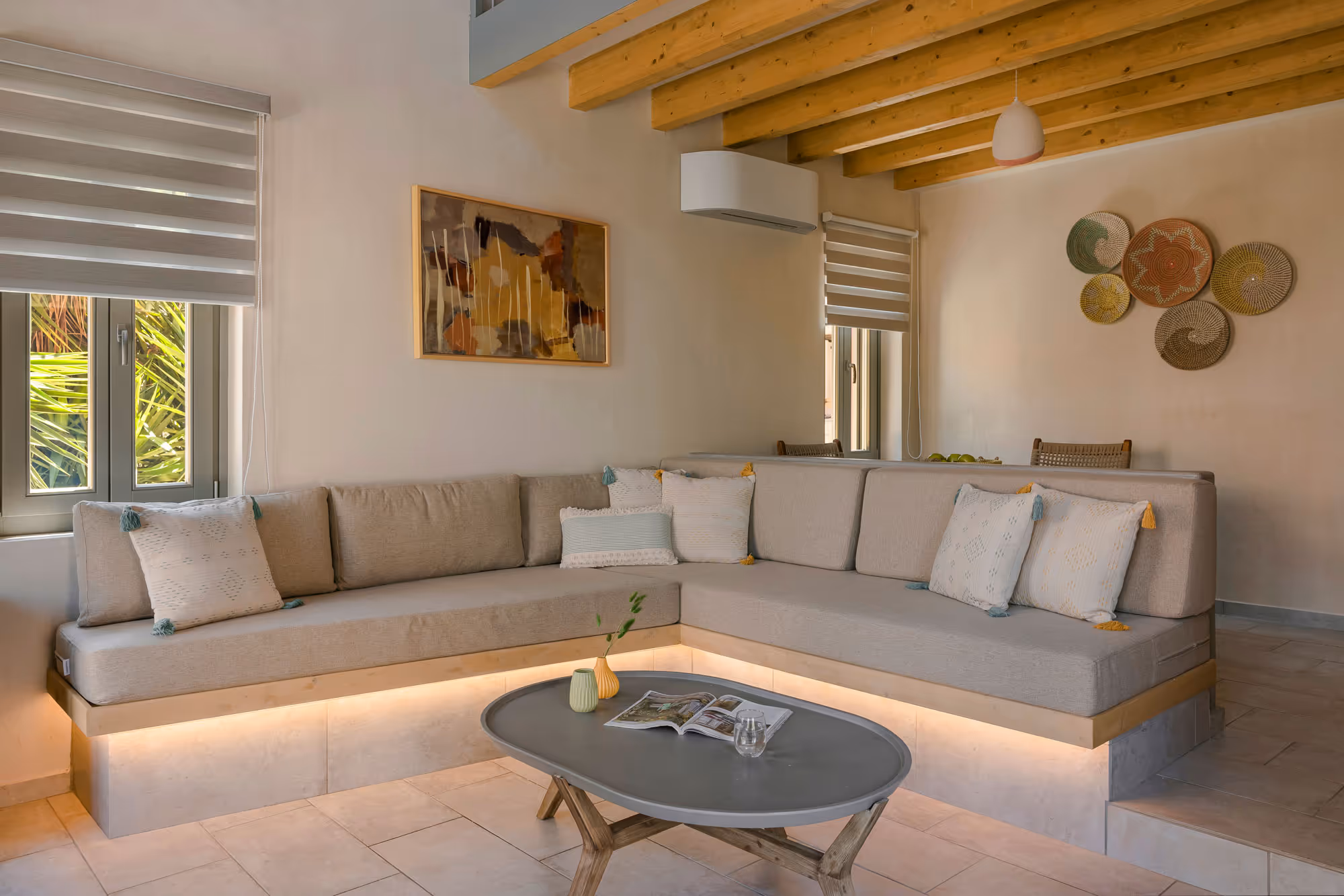 Modern beige L-shaped sofa with cushions and under-lighting in a cozy living room with wooden beams.