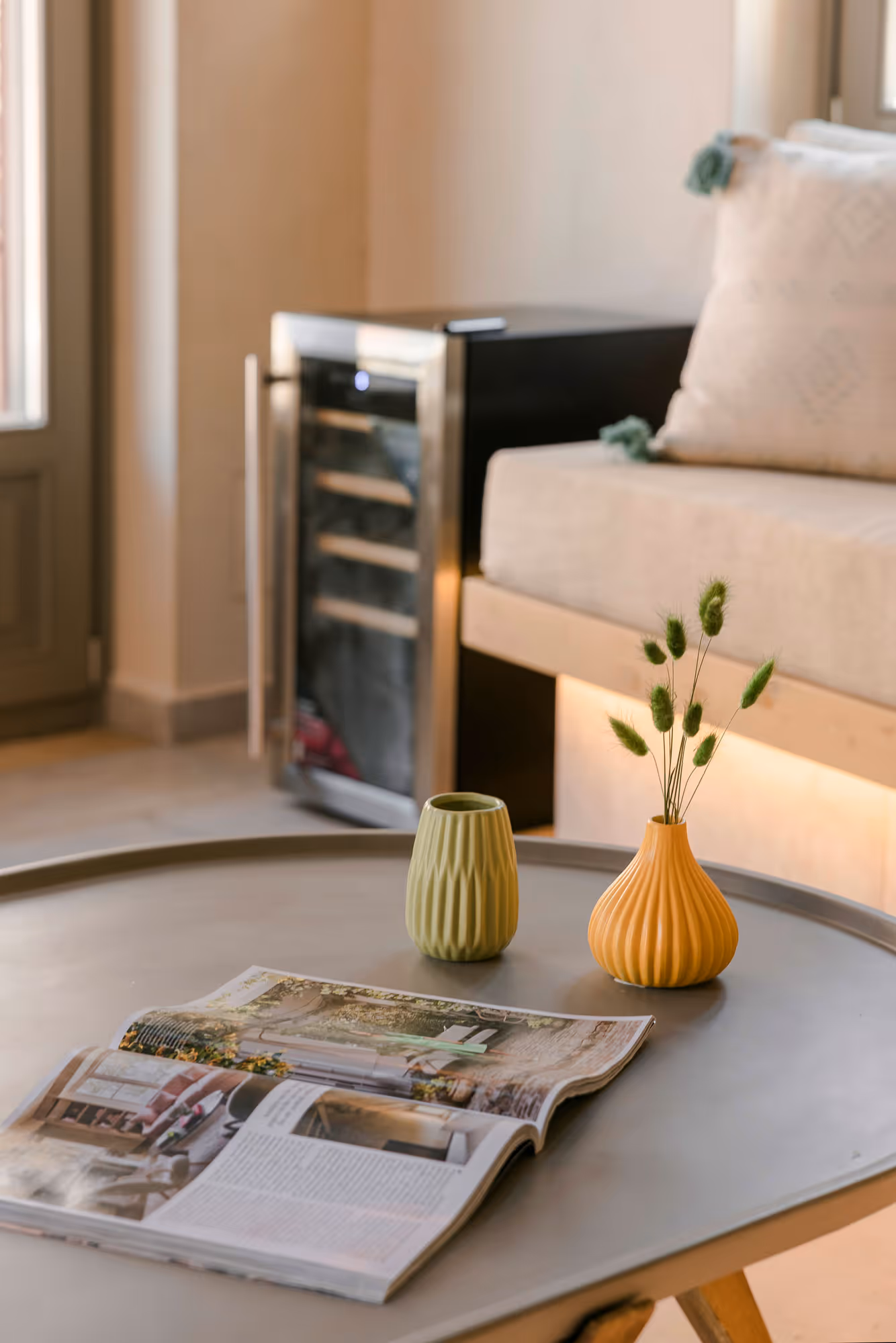 Round table with an open magazine and two small decorative vases, one orange with greenery inside.